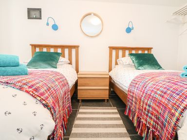A bedroom with two single beds with colorful throws and green pillows a wooden nightstand between the beds and a round mirror on the wall at Gull Rock in Trebarwith Strand