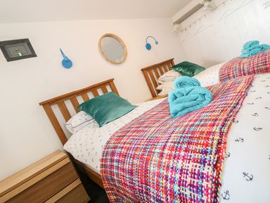 A bedroom with two wooden single beds colorful blankets blue towels and green pillows at Gull Rock in Trebarwith Strand