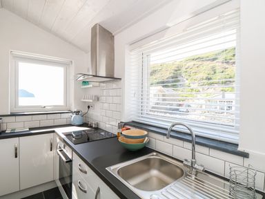 A kitchen with a sink stove oven and kettle by windows with mountain views at Gull Rock Trebarwith Strand