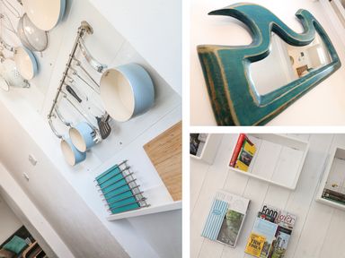 A kitchen wall with hanging pots and utensils a wooden mirror with a blue frame and a white floor with magazines and books on shelves at Gull Rock in Trebarwith Strand