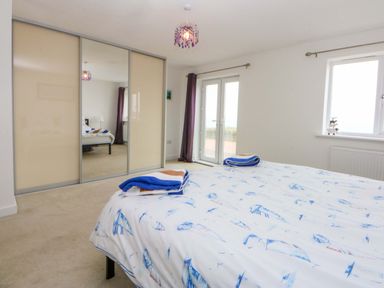 A bedroom featuring a bed with bedding and mirrored wardrobe at Welymora in Pwllheli