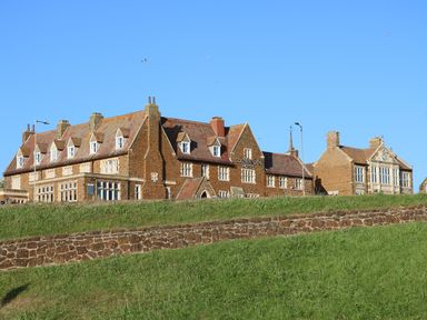 A large brick building with multiple chimneys and windows on a grassy hill at Tillys Retreat in Hunstanton