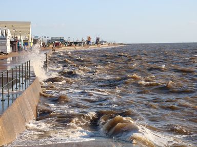 A sea wall with waves crashing against it and a promenade with people and buildings at Tilly's Retreat in Hunstanton