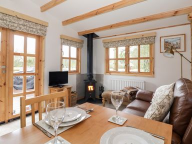 A small living room with a wood stove television dining table and leather sofa at Someplace Else in Diss