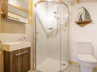 A bathroom with a curved glass shower enclosure a sink with wooden cabinet and a toilet with sailboat wall decoration at Someplace Else in Diss