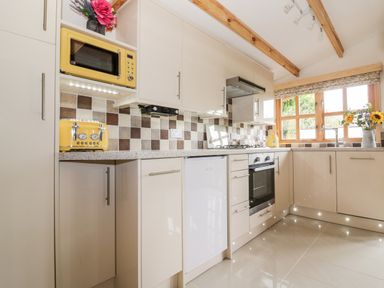 A kitchen with white cabinets yellow microwave toaster and kettle tiled backsplash and wooden window at Someplace Else in Diss