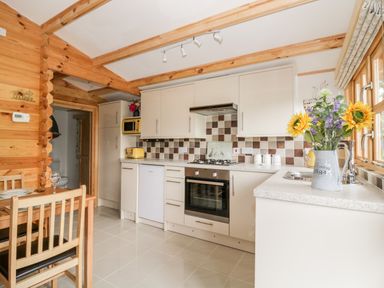 A kitchen with cream cabinets a tiled backsplash and a sunflowers bouquet in a jug at Someplace Else in Diss