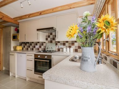 A kitchen with beige cabinets a gas stove a yellow toaster a microwave a vase with sunflowers and other flowers on the counter at Someplace Else in Diss