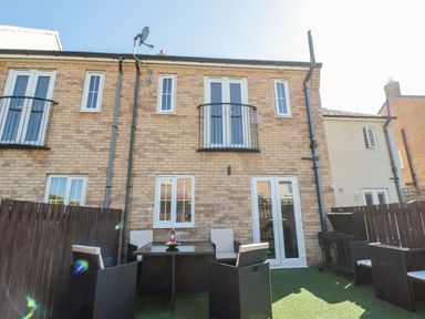 A backyard with a table and chairs on artificial grass behind a brick house at Beach House in Beadnell