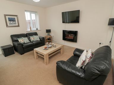 A living room with two black leather sofas a wooden coffee table mugs on the table a wall-mounted TV and electric fireplace at Beach House in Beadnell