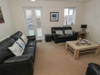 A living room with two black leather sofas a wooden coffee table with cups and plates and a side table with a lamp at Beach House in Beadnell