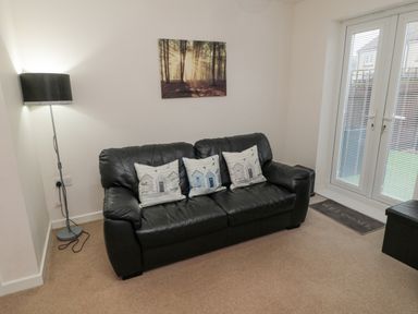 A black leather sofa with three decorative pillows a floor lamp a wall painting and glass doors with blinds at Beach House in Beadnell