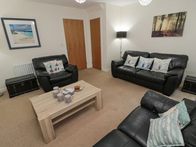 A living room with black leather sofas cushions a wooden coffee table with cups and plates two doors and framed wall art at Beach House in Beadnell