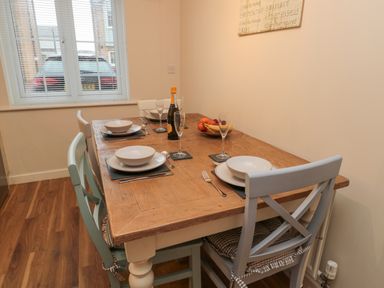 A dining room with a wooden table set for four with plates glasses and a bottle next to a window at Beach House in Beadnell