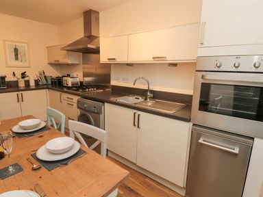 A kitchen with a wooden dining table set with plates and cutlery near a counter with a sink oven washing machine and cooking appliances at Beach House in Beadnell