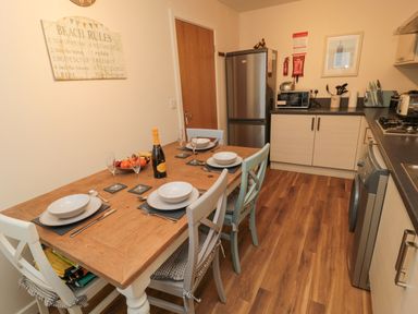 A kitchen with a wooden dining table set with plates glasses and cutlery and a sign on the wall at Beach House in Beadnell