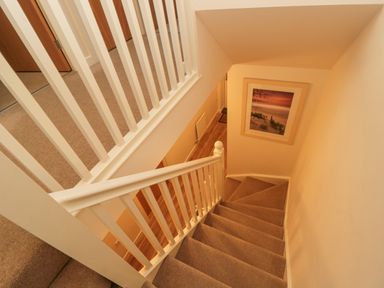 A carpeted staircase with white handrails and a framed beach sunset picture on the wall at Beach House in Beadnell
