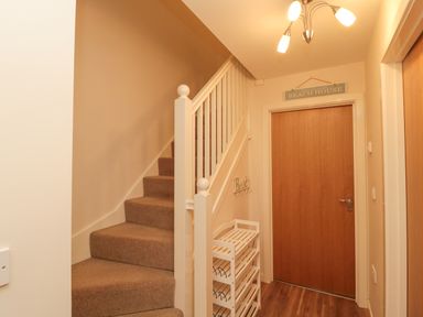 A hallway with carpeted stairs a wooden door a white shoe rack and a light fixture at Beach House in Beadnell