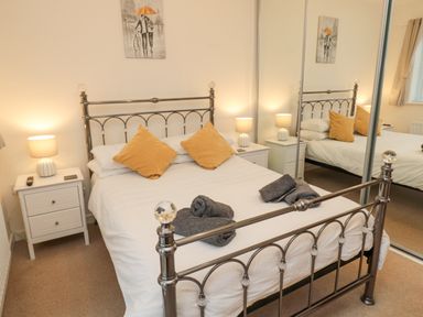 A bedroom with a metal bed frame white bedding two yellow pillows two bedside tables with lamps and mirrored wardrobe doors at Beach House in Beadnell