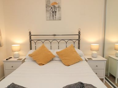 A bedroom with a metal headboard bed two orange pillows two white bedside tables with lamps and a painting on the wall at Beach House in Beadnell