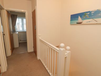 A hallway with beige carpet and white railing with a nautical painting on the wall at Beach House in Beadnell