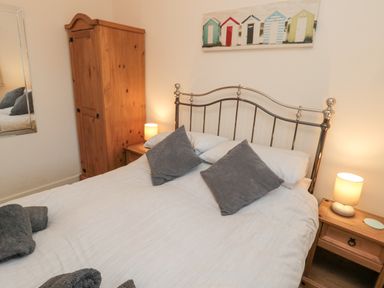A bedroom with a double bed metal headboard wooden nightstands lamps wardrobe and a wall painting at Beach House in Beadnell