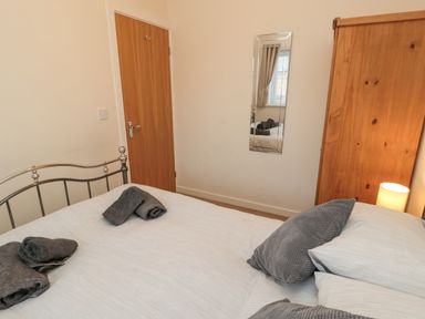 A bedroom with a bed with gray towels and pillows a wooden door a wardrobe and a wall mirror at Beach House in Beadnell