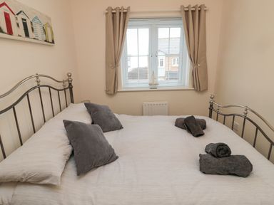 A bedroom with a metal bed frame pillows towels and a window with curtains and blinds at Beach House in Beadnell