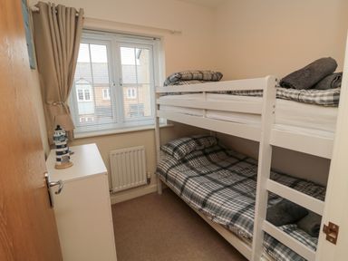 A small bedroom with bunk beds a window a white chest of drawers and a lighthouse decoration at Beach House in Beadnell