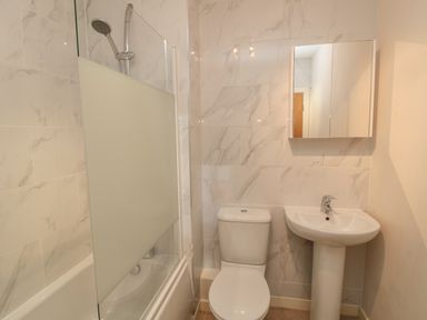 A bathroom with a toilet sink bathtub and shower with frosted glass panel at Beach House in Beadnell