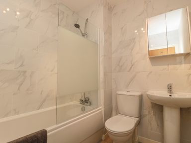 A bathroom with a bathtub and shower, toilet, pedestal sink, and mirrored cabinet at Beach House in Beadnell