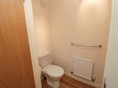 A small bathroom with a toilet a radiator a towel rail and a wooden floor at Beach House in Beadnell