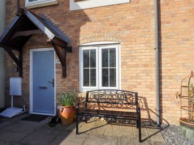 A blue front door with a small roof above and a black metal bench with welcome sign outside a brick house
