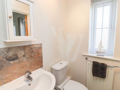 A bathroom with a sink and faucet a toilet a window with blinds and a model sailboat a towel hanging on a radiator at Beach House in Beadnell