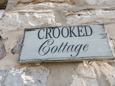 A wooden sign with the text Crooked Cottage on a stone wall at Crooked Cottage in Kirkbymoorside