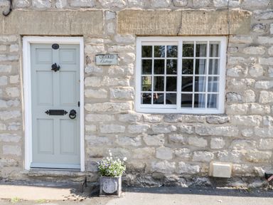 A stone cottage wall with a pale blue door and a window beside it with a flower pot outside at Crooked Cottage in Kirkbymoorside