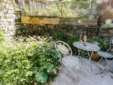 An outdoor patio with white metal table and chairs surrounded by stone and wooden walls with plants at Crooked Cottage in Kirkbymoorside