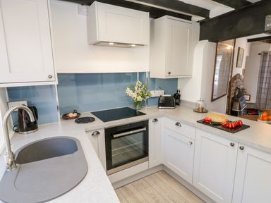 A kitchen with white cabinets a sink an oven a toaster and bread with tomatoes on the counter at Crooked Cottage in Kirkbymoorside
