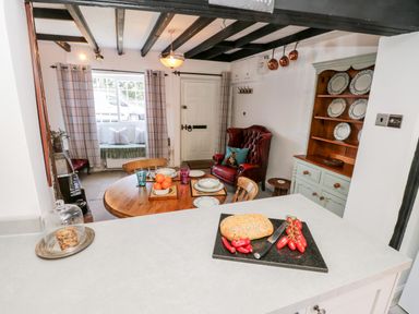A kitchen and dining area with a round wooden table set for four chairs and a red leather armchair at Crooked Cottage in Kirkbymoorside