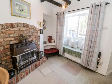 A sitting area with a brick fireplace bench with cushions and a window with curtains at Crooked Cottage in Kirkbymoorside