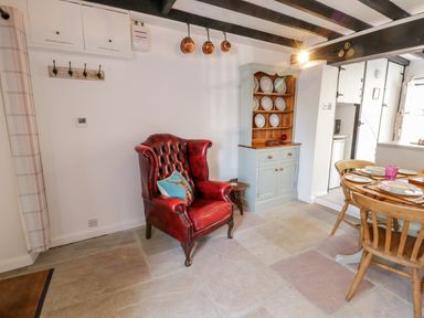 A dining area with a red leather armchair a cabinet with plates and a wooden dining table with chairs at Crooked Cottage Kirkbymoorside