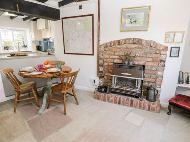 A dining area with a round wooden table and three chairs next to a brick fireplace and an open kitchen at Crooked Cottage in Kirkbymoorside