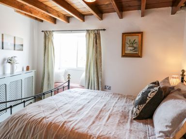 A bedroom with a bed a window seat curtains and a painting at Crooked Cottage in Kirkbymoorside