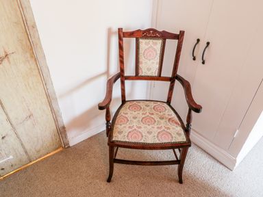 A wooden armchair with floral patterned upholstery in a room with a wardrobe and wooden door at Crooked Cottage in Kirkbymoorside