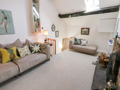 A living room with two beige sofas and pillows near a fireplace and staircase at Crooked Cottage in Kirkbymoorside