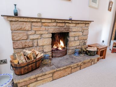 A stone fireplace with firewood and fire tools in a living room at Crooked Cottage in Kirkbymoorside