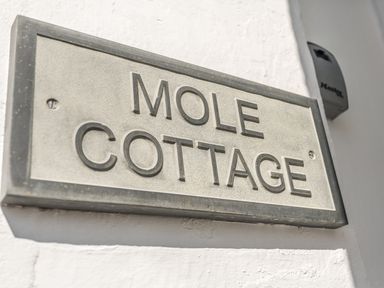 A sign on a white wall displaying Mole Cottage in Mousehole