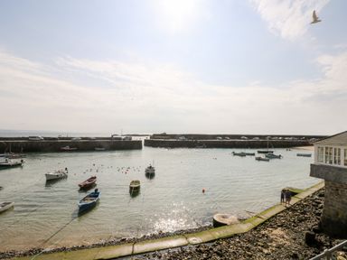 A harbor with small boats in the water and a stone pier with cars and people near Mole Cottage in Mousehole