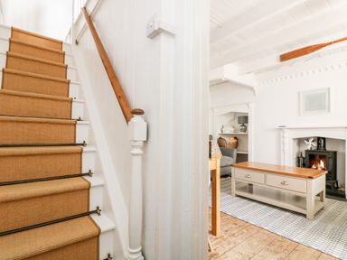 A staircase with a carpet runner next to a living room with a coffee table and a fireplace at Mole Cottage in Mousehole