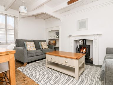 A living room with gray sofas a wooden coffee table a fireplace and a patterned rug at Mole Cottage in Mousehole